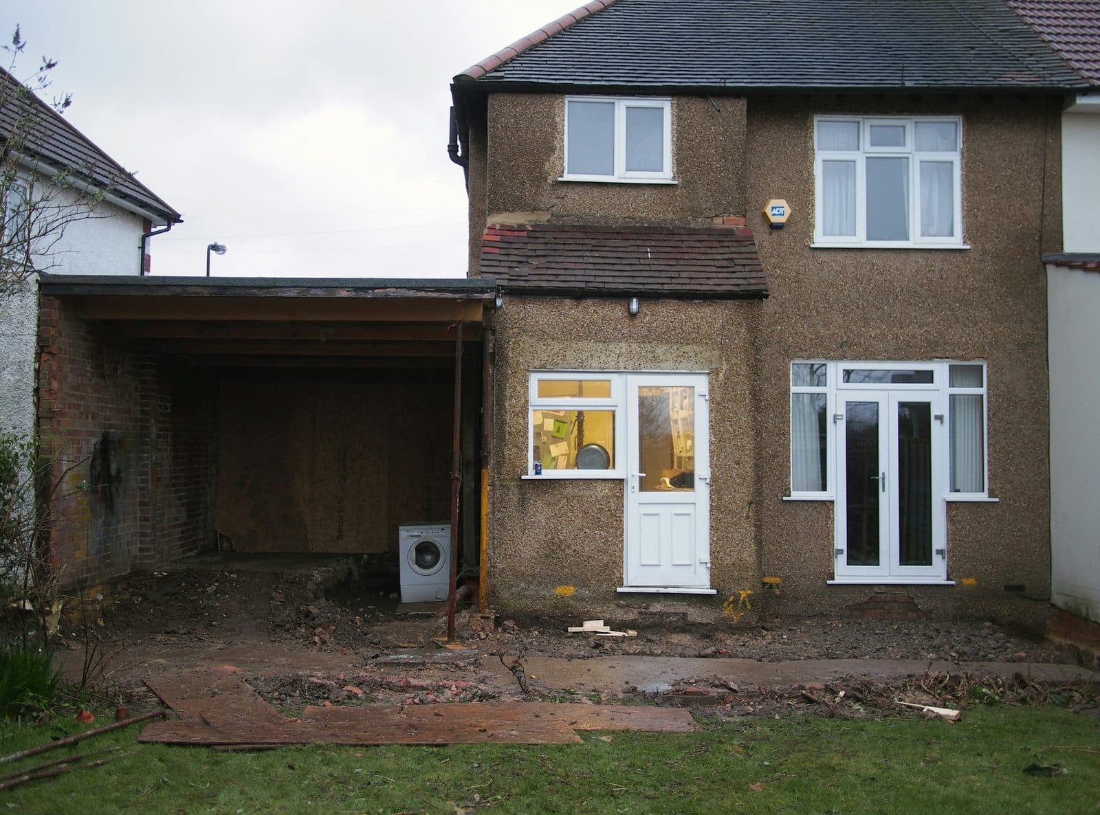 Back of a house before renovation with an open lean-to and torn-up patio