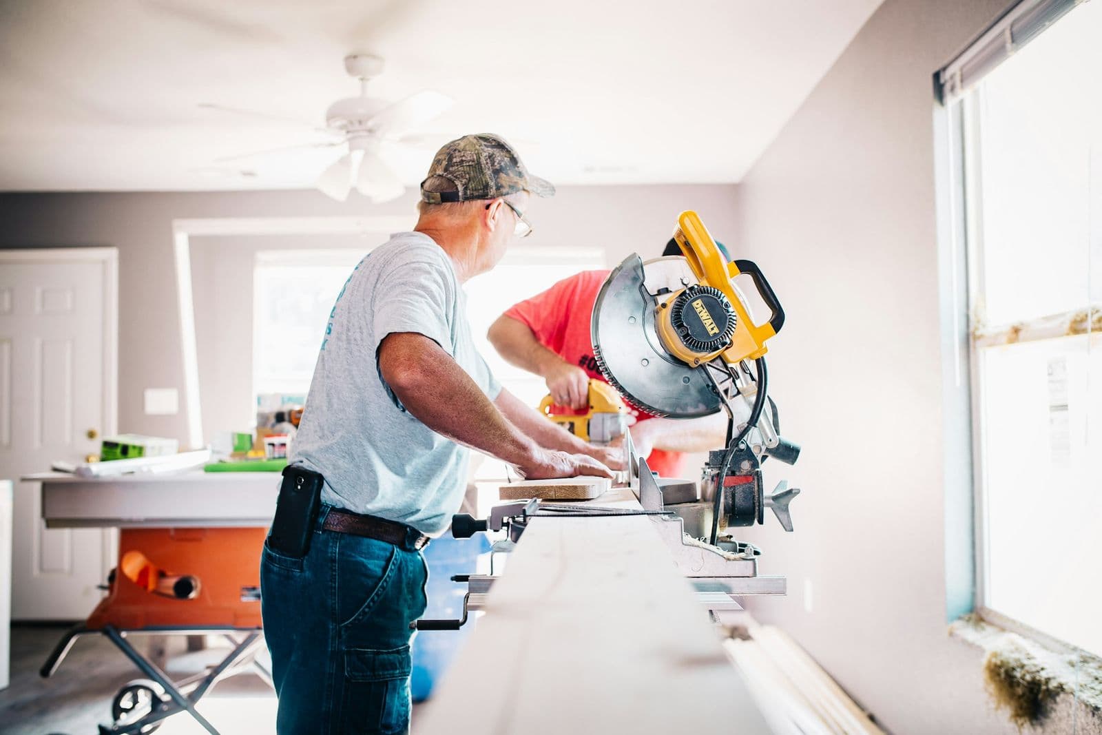 Carpenter cutting trim on a miter saw inside a bright room under renovation